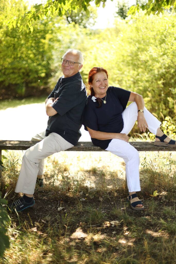 Axel und Ursula Höltge Rücken an Rücken gelehnt auf einem Holzbalken in der Natur