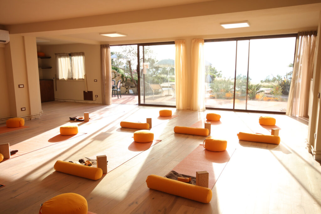 Heller lichtdurchfluteter Yogaraum mit orangen Yogamatten und Sitzkissen