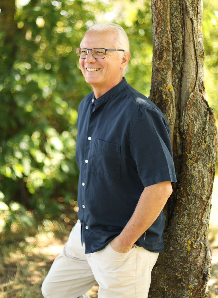 Axel Höltge in dunkelblauem Hemd angelehnt an einem Baum