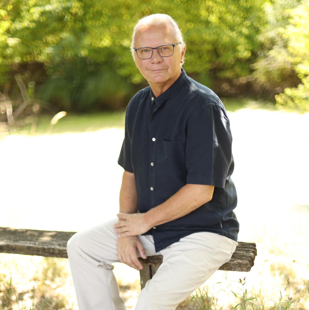 Axel Höltge sitzt auf einem Holzbalken in der Natur